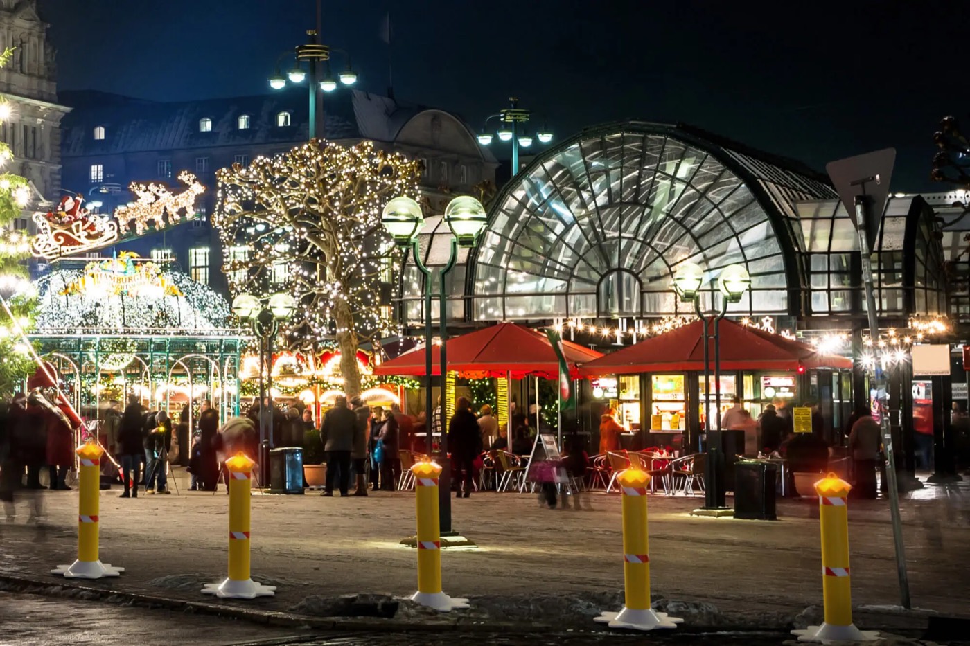 Gelbe Poller-Sperren vor einem beleuchteten Weihnachtsmarkt am Abend